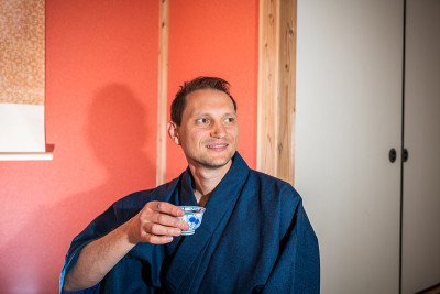 传统的日本屋町屋客栈与年轻人快乐的脸拿着杯在和服在红色的壁龛喝绿茶