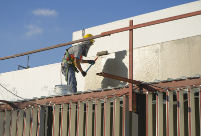 建筑工人在高层建筑外立面用滚轴涂漆