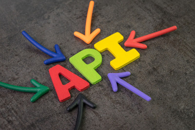 API，应用程序编程接口概念，多色箭头指向字API在黑色水泥黑板墙的中心，桥梁连接和发送应用程序之间