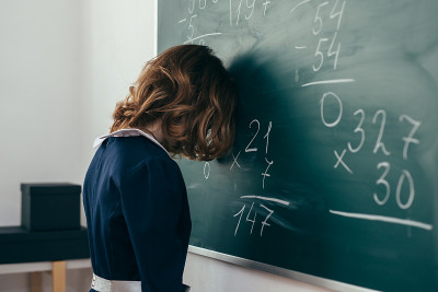 悲伤的女学生试图解答一个例子。一个女生站在黑板上，额头贴着黑板