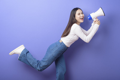 年轻美丽的微笑女人的肖像是用扩音器宣布在孤立的紫色背景演播室