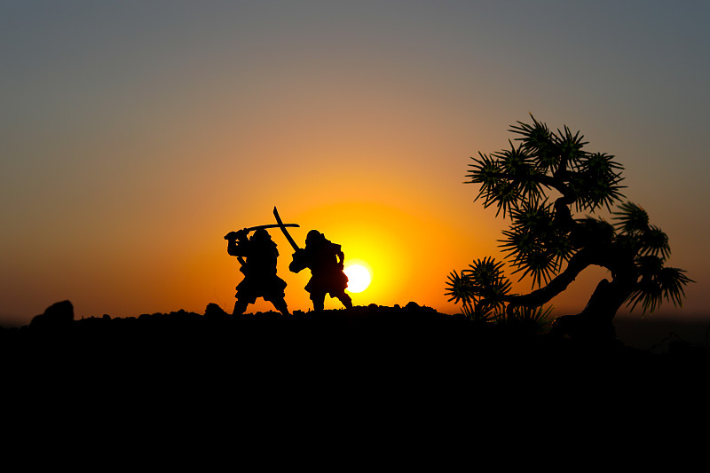 两个武士决斗的剪影。画上两个武士和日落的天空。有选择性的重点