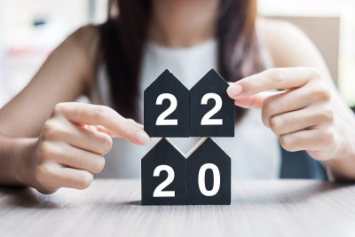 年轻的女商人手握2022年新年快乐与房子模型桌上的办公室。新房，金融，财产保险，房地产，储蓄和新年决