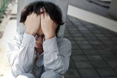 正面视图的悲伤沮丧的年轻亚洲商人盖着脸与手。