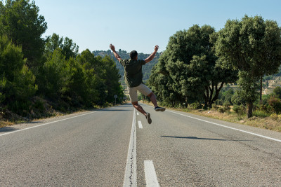 男人在空旷的路上跳跃。世界观光旅行家