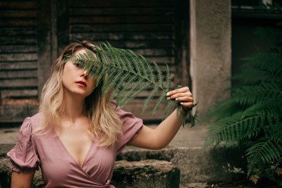 一个年轻的女人手里拿着蕨叶，遮住了脸的一部分。天然化妆品的概念，乡村生活