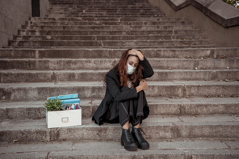 新冠肺炎带来的失业。沮丧的女商人戴着口罩，在办公室外与私人职员包厢感到绝望后，由于冠状病毒裁员裁员裁