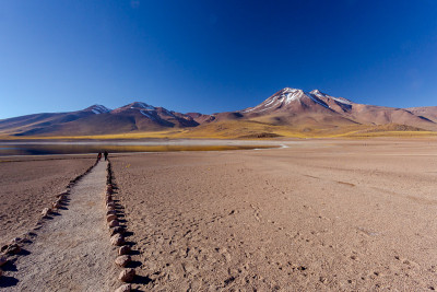 两个人走向湖在拉古纳米斯坎蒂和Miñiques火山。位于智利阿塔卡马沙漠的弗拉门戈斯国家保护区