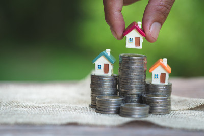 女人的手把房子模型放在硬币堆上。Concept for property ladder，规划攒钱买房