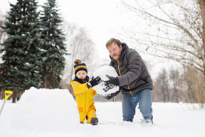 小男孩和他的父亲在下雪的公园堆雪人。冬季与孩子们一起进行户外活动。