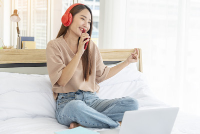 放松女人拿着书在床上用耳机听音乐。少妇放松阅读，翻开书本，休闲心灵。幸福美丽的女人人