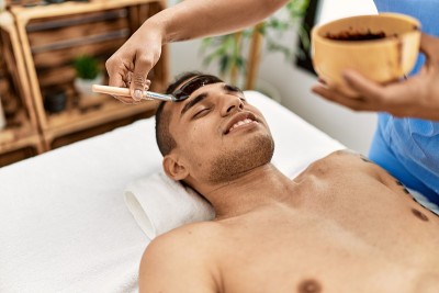 拉丁男子微笑愉快地接受美容中心的面部护理。
