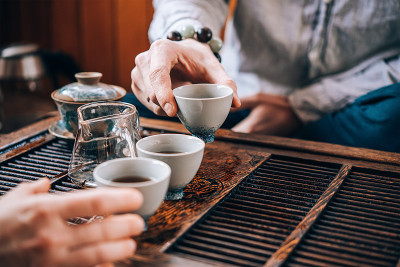 两个人坐在茶道桌旁边的地板上，朋友们一边喝茶一边聊天，桌上放着中国茶道用的白色陶瓷茶杯和玻璃茶壶