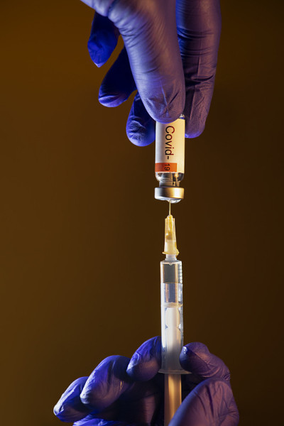 戴着蓝色手套的手用注射器抽新冠疫苗