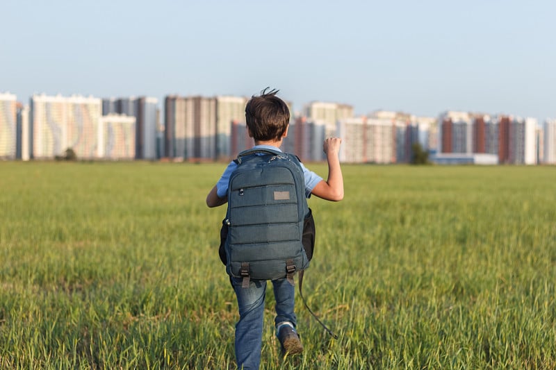 在城市风景的映衬下，小学生背着书包在操场上快乐地奔跑