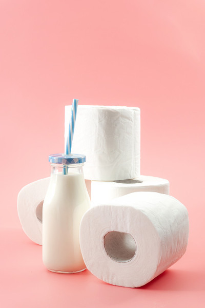 乳糖不耐症和无法消化牛奶的概念主题与一瓶牛奶与蓝色的吸管和一卷卫生纸孤立在粉红色的背景