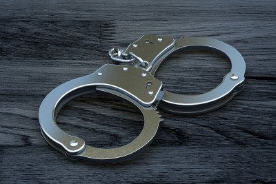 刑事司法与有罪判决理念:桌上钢手铐。黑色木制背景上的警察金属手铐