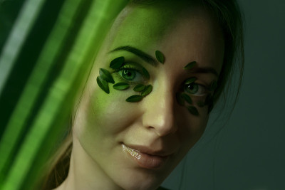 或年轻女子的特点与自然化妆散焦的火花。绿叶贴在脸上。草药的概念。