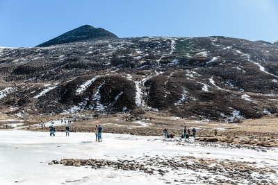 黑山下有雪，游客在地上有棕色的草，雪和结冰的池塘在冬天在零点拉冲。北锡金,印度。