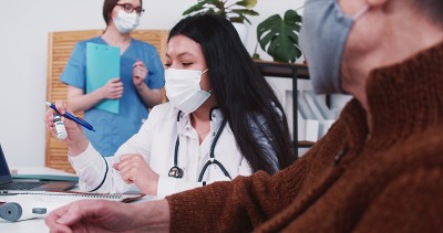 混血药房女医生在门诊检查时将装有疫苗药物的烧瓶给资深白种病人女。