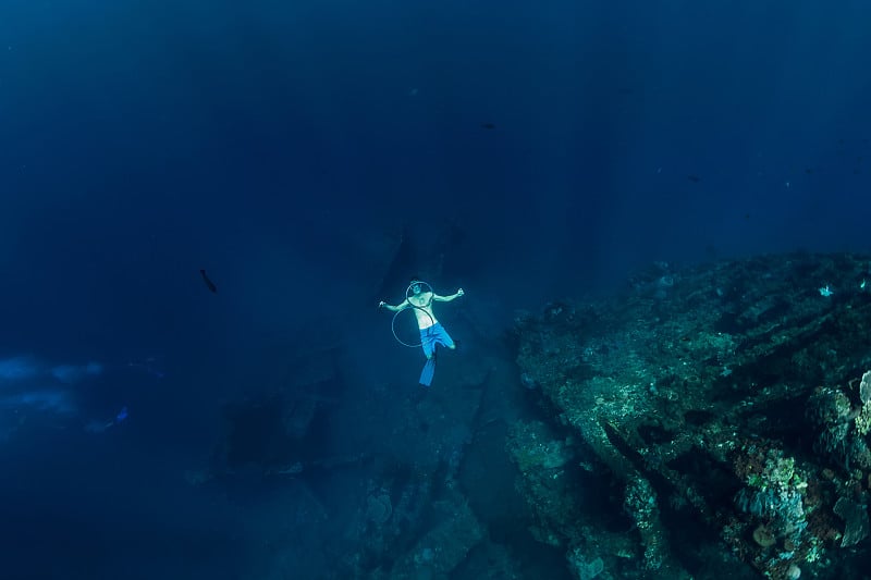 自由的潜水员在深水中在沉船附近制造环状气泡