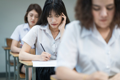 选择重点十几岁的大学生坐在讲座椅上做期末考试，并在试卷上写下答题纸。学生们在教室里穿着校服。