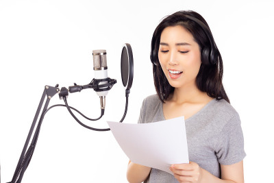 女歌手在录音室里通过读纸条来唱歌，用麦克风，流行滤镜来录制音乐。女歌手在录音室里孤立的白色背景下表演