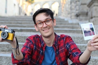 可爱的潮男拿着复古相机和即时胶卷照片
