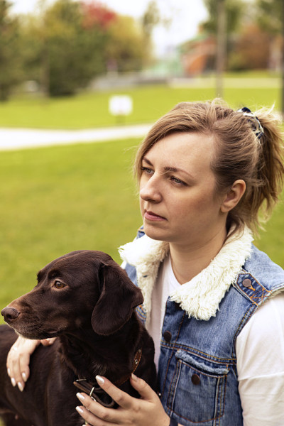 快乐的年轻女人金发和牛仔背心拥抱一只西班牙猎犬。