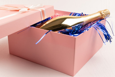 a gold bottle of champagne lies in a pink box with