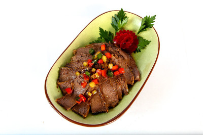 在一个椭圆形的盘子里，放上几块深色的肉，配上香菜叶和甜菜，这是中国菜，背景很亮。