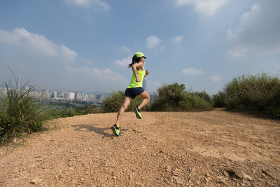 女超级马拉松运动员在现代城市旁边的山上跑步