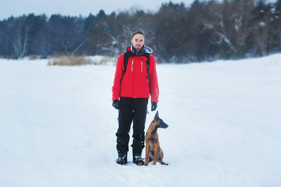 一个男人和比利时牧羊犬在冬天。下雪的背景。冬季森林