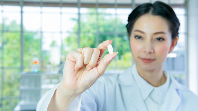 科学家在实验室。妇女研究拿着白色药丸药丸与白色长袍站与脸集中。与背景室内白色实验室。