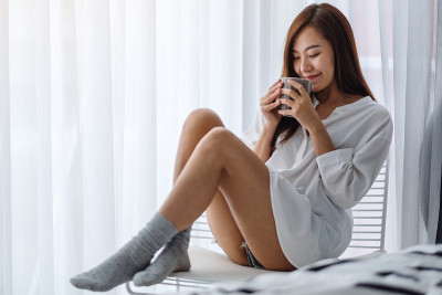 早上在家里的白色卧室里喝着热咖啡的女人