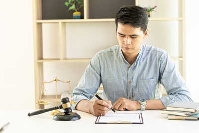 年轻的亚洲律师一边在办公室工作，一边从事财务审计和客户支持工作。将锤子和天平放在你面前，代表法律概念