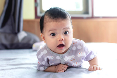 东南亚的新生婴儿正在地板上爬行。新生儿穿着灰色衬衫。宝宝是东南亚人。孩子是可爱的。孩子在室内拍照。婴