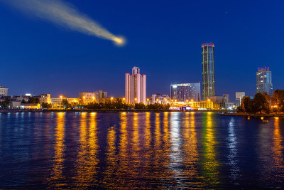 彗星在城市摩天大楼上方的夜空中。河中的倒影