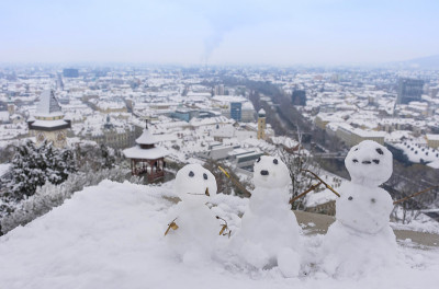 在奥地利斯蒂里亚地区格拉茨的冬日里，有三个有趣的雪人和施洛斯堡山上著名的钟楼。有选择性的重点