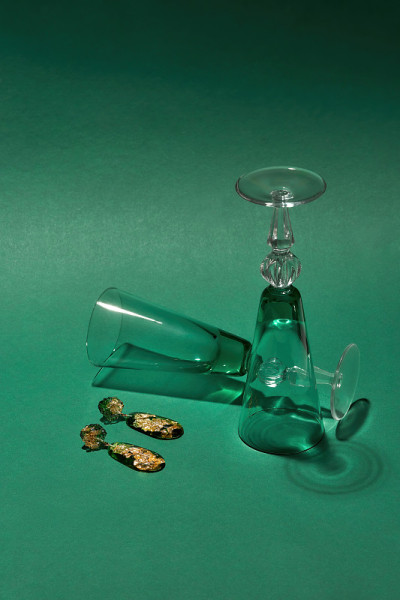 工作室拍摄了时髦的手工环氧树脂耳环，里面有金箔，两个葡萄酒杯被隔离在绿色背景上