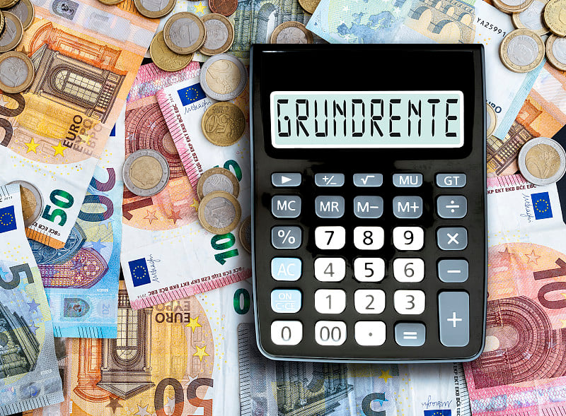 在袖珍计算器上显示的德语单词GRUNDRENTE(基本养老金)与桌上的现金相对