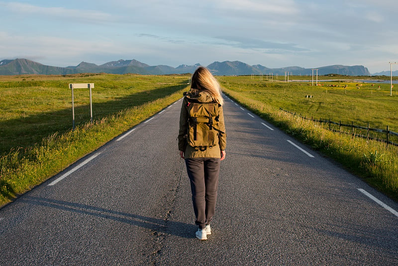 一个金发女人走在空荡荡的路上。女孩等待。寻找一条新的道路。搭便车旅行。旅行、冒险。感受自由，享受放松