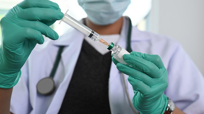 医生在医院里戴着防护口罩，拿着注射器从药瓶里取出液体疫苗准备注射。