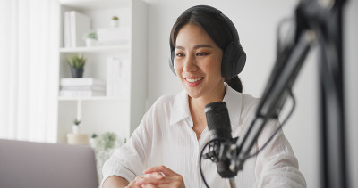 一名年轻的亚洲女性在家庭录音室用笔记本电脑录制播客。