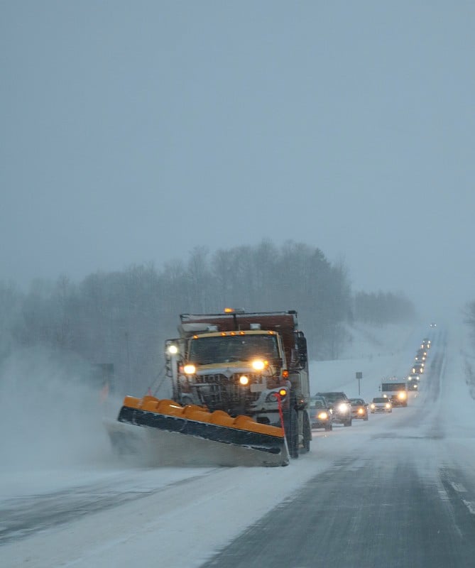 扫雪机在狂风中移动着道路上的积雪，后面跟着一辆辆汽车