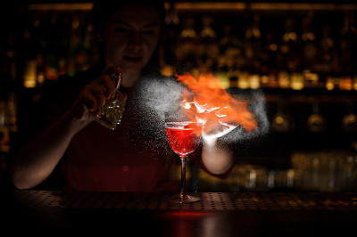女调酒师往鸡尾酒上喷洒，然后把它点着了