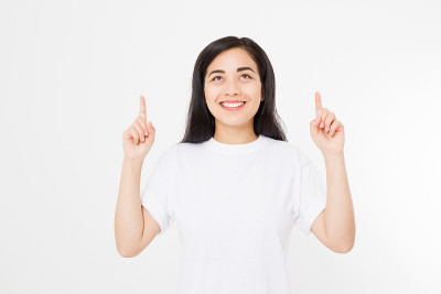 微笑的年轻亚洲女人的肖像穿着夏季t恤指着拷贝空间由手指孤立在白色模板和空白背景。