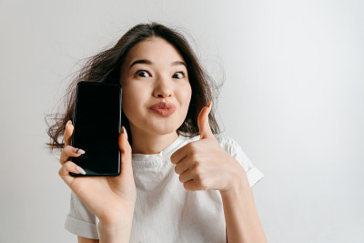 一个自信随意的亚洲女孩的肖像显示空白的手机屏幕