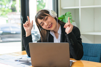 年轻的亚洲女性喜欢听音乐戴着耳机感觉放松的办公桌。