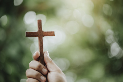 靠近基督教男子的双手捧着一个神圣的十字架和崇拜祈祷上帝与自然的背景。基督徒敬拜祈祷神的观念。
